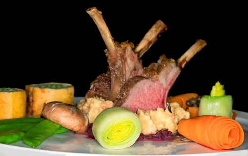 Pink roasted saddle of lamb on corn polenta with red wine onions and various vegetables