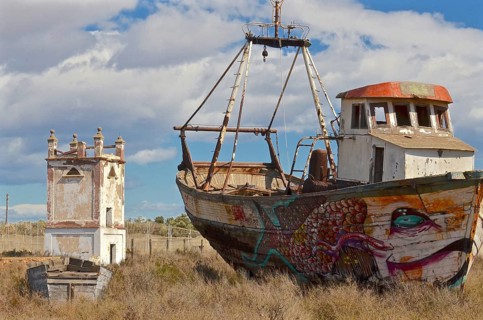 Painted wreck of fishing boat in front of old pigeon tower