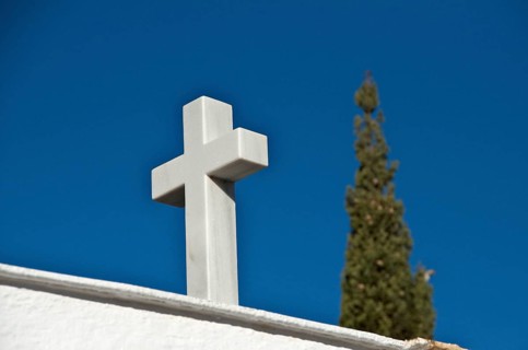White marble cross in front of cypress tree in cemetery