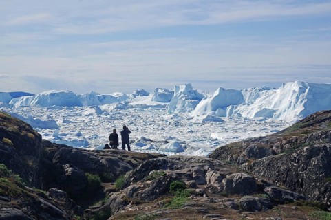 People sitting in front of fjord covered with ice and icebergs