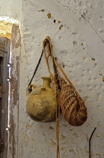 Clay drinking vessel with bag of esparto grass on nail in front of white wall