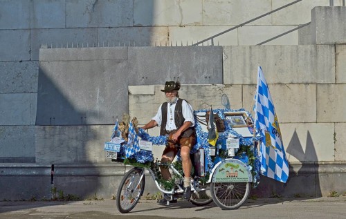 Man in Bavarian traditional costume on Bavarian decorated bicycle with white-blue Bavarian flag