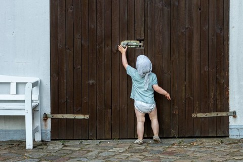 Toddler tries to move the security latch on a wooden door