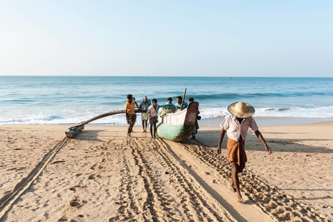 Fishermen pull fishing boat out of the sea onto the sandy beach