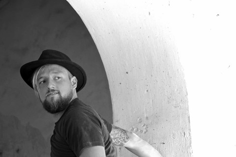 Young man with beard and black hat looks around questioningly
