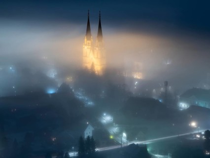 Illuminated church towers of Admont Abbey rise out of the fog