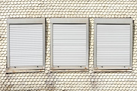 Closed plastic roller shutters in wooden historic facade made of wooden shingles