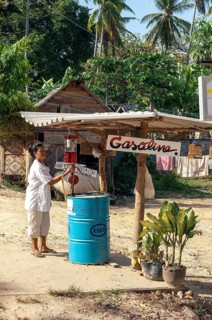 Thai woman operates rural simple petrol station with large gasoline barrel for gasoline on remote country road
