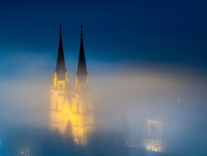 Illuminated church towers of Admont Abbey rise out of the fog