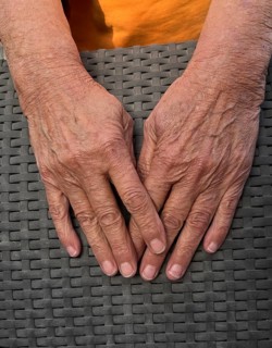 Wrinkled hands of an old woman on wickerwork of wicker chair