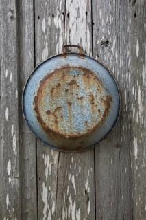 Old rusted pan hanging on grey weathered wall of old rustic wood plank cabin