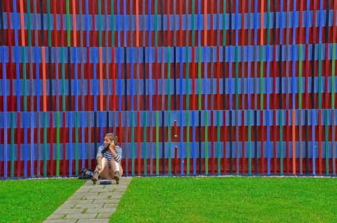 Young woman on the phone sitting on the floor in front of the colourful striped facade of the Museum Brandhorst