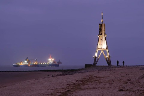 Illuminated Kugelbake and illuminated ship at blue hour