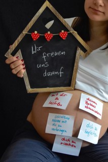 Expectant with wish list on belly holds up black board