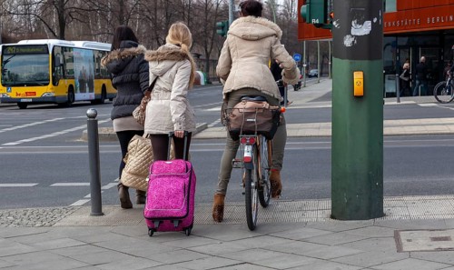 Pedestrians and cyclists with luggage standing at a traffic light