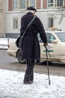 Senior citizen with walking stick in winter road conditions