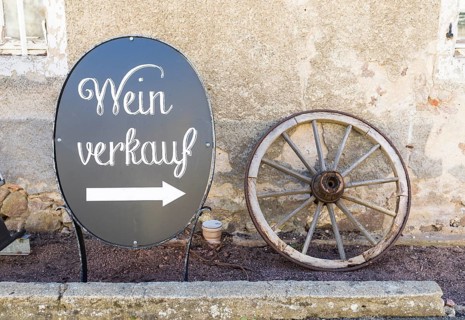 Board with arrow for wine sale and old wagon wheel as decoration at Weinhaus Schuh