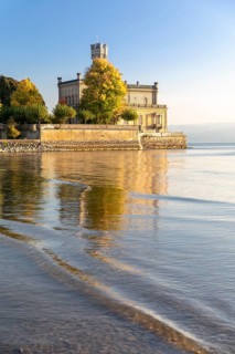 Autumn trees on the shore in the sunshine with Montfort Castle