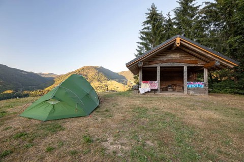 Green tent near hut on dry summer meadow