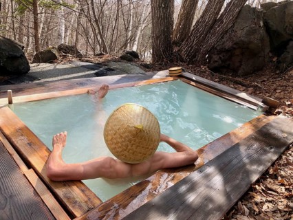 Young man with Japanese hat bathes in an onsen