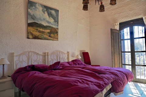 Bedroom with upholstered double bed and oil painting in front of open shutters