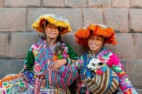 Two Inca woman in traditional traditional costume with lambs in front of an Inca wall