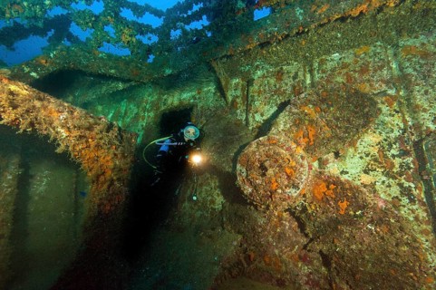 Diver looks at illuminated replacement propeller on deck of wreck of sunken cargo ship M/V M/N Kent