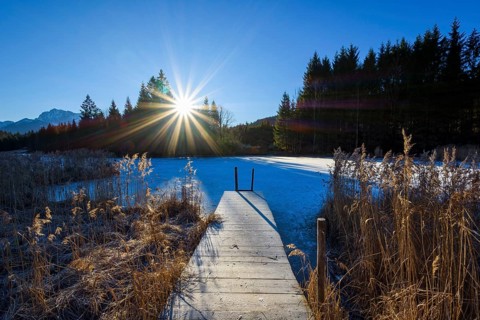 Wooden jetty with frozen lake and sun