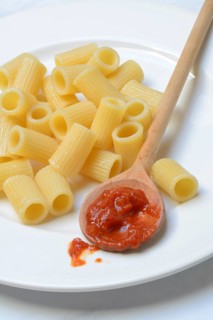 Cooked rigatoni and cooking spoon with tomato sauce