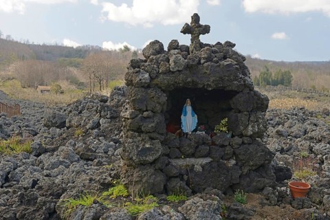 Lava rock and statue of the Virgin Mary at the foot of Mount Etna