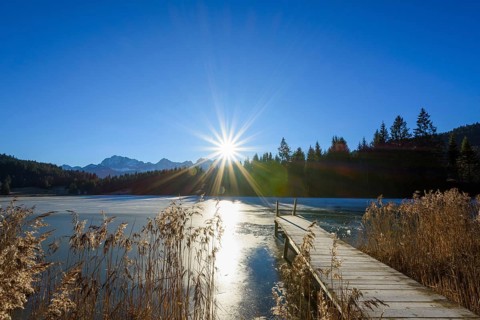 Wooden jetty with frozen lake and sun