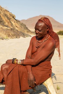 Himba woman resting at the bank of the dry river bed of the Hoarusib river