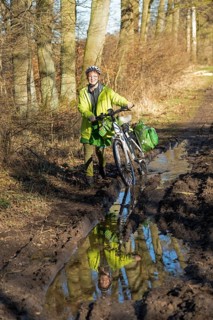 Woman cycling with e-bike over muddy forest path and through puddles