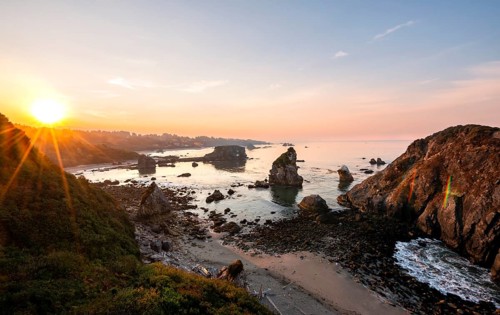 View of sea and sandy beach Harris Beach with rocks at sunrise with sun star