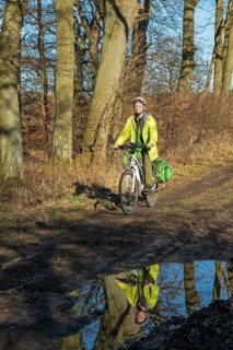 Woman cycling with e-bike over muddy forest path and through puddles