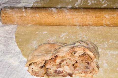 Rolling pin and a piece of apple strudel with sultanas lie on a strudel dough