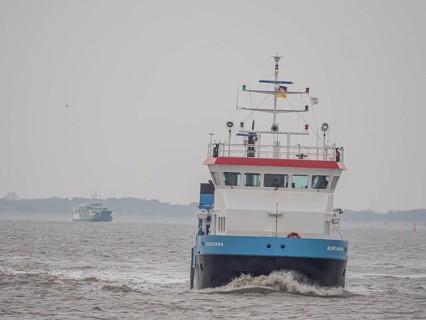 Supply ship Burchana with ferry Spiekeroog IV on the stormy North Sea entering the harbour