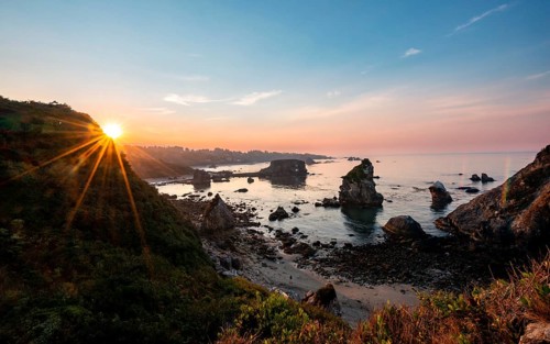 View of sea and sandy beach Harris Beach with rocks at sunrise with sun star