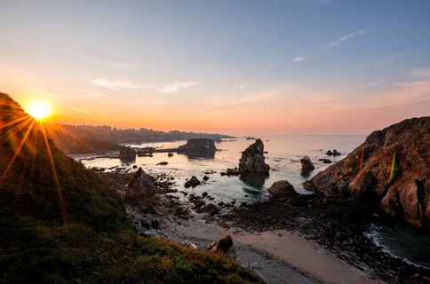 View of sea and sandy beach Harris Beach with rocks at sunrise with sun star