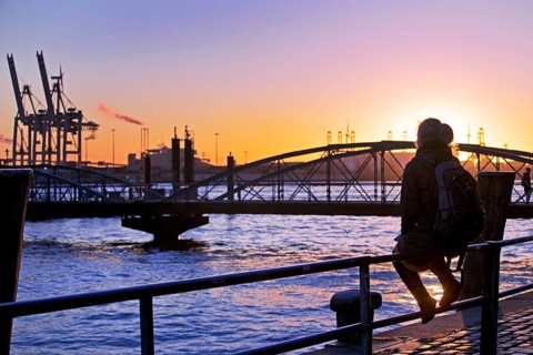 A woman sits on a railing at sunset on the Norderelbe in Altona