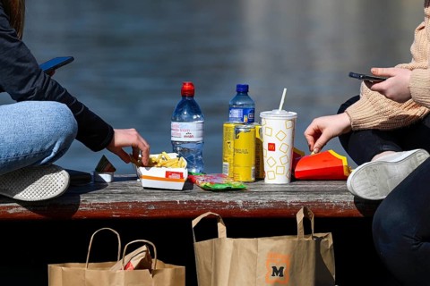 Teenagers with smartphones eat take away from McDonalds at the lake