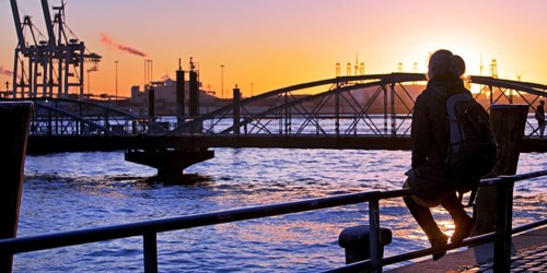 A woman sits on a railing at sunset on the Norderelbe in Altona
