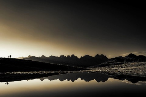 Salfainsee with reflection of the Kalkkoegel and mountaineers on mountain meadow at sunrise
