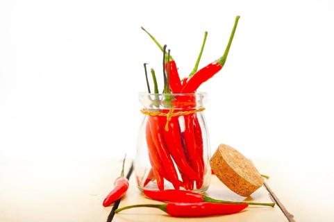 Red chili peppers on a glass jar over white wood rustic table