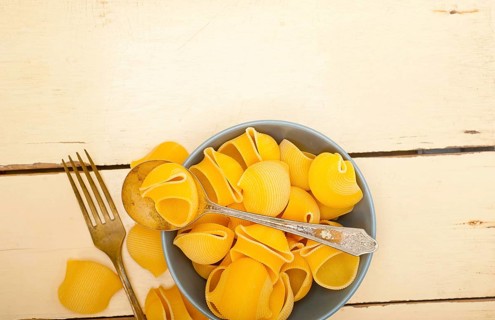 Raw Italian snail lumaconi pasta on a blue bowl over rustic table macro