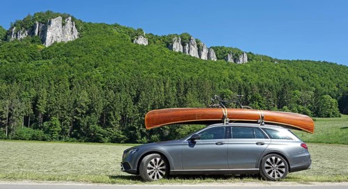 Mercedes with cedar wood canoe on roof in front of rocks in the Danube valley