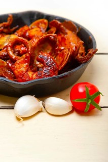 Fresh seafood stew prepared on an iron skillet ove white rustic wood table