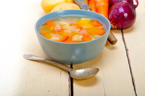 Traditional Italian minestrone soup on a rustic table with ingredients