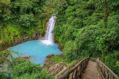 Many steps lead down to the waterfall with blue turquoise water of the Rio Celeste