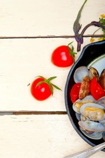 Fresh clams stewed on an iron skillet over wite rustic wood table